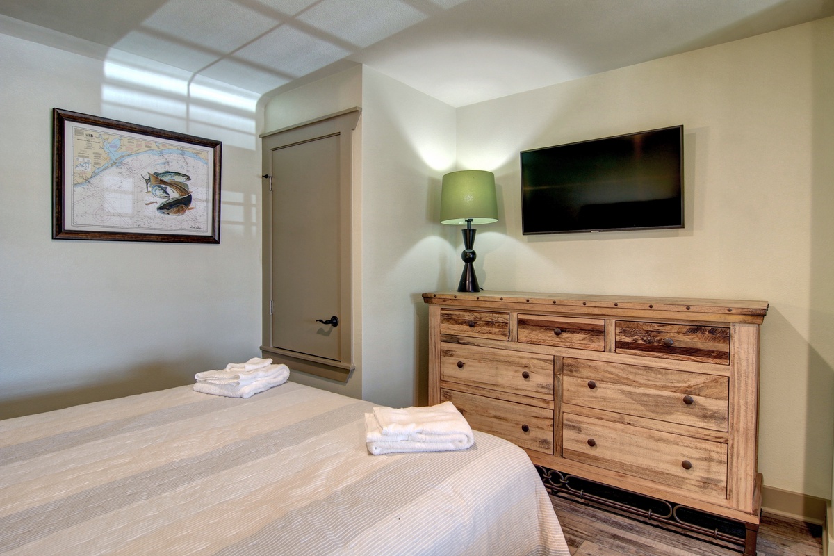 Your cozy bedroom features a warm wood dresser, flat-screen TV, and fresh towels awaiting your arrival.