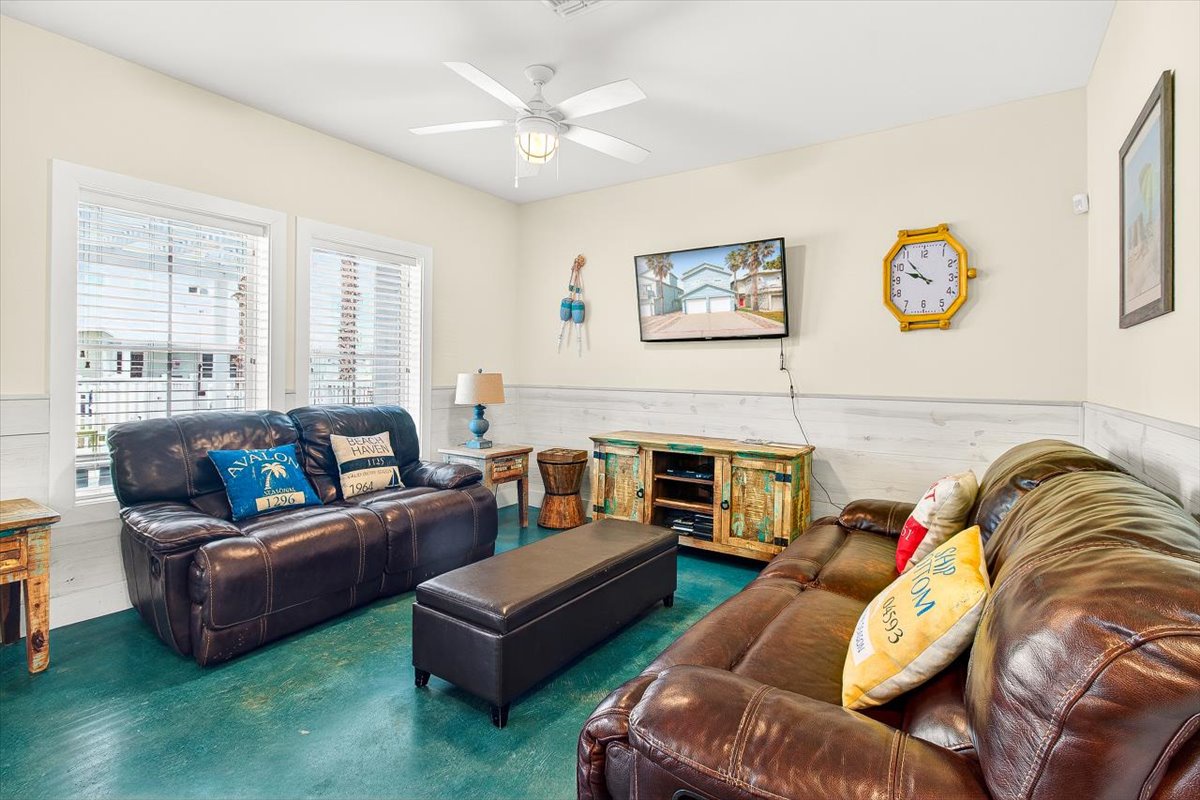 Sink into plush leather sofas in your spacious second living area, where coastal vibes meet comfort beneath a cooling ceiling fan.