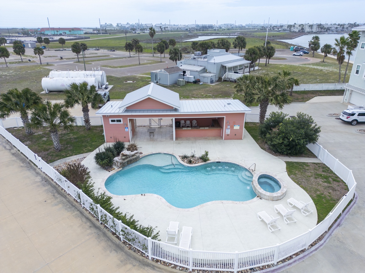 Aerial view of coral-colored vacation rental with private pool, hot tub, and tropical landscaping in coastal community setting.