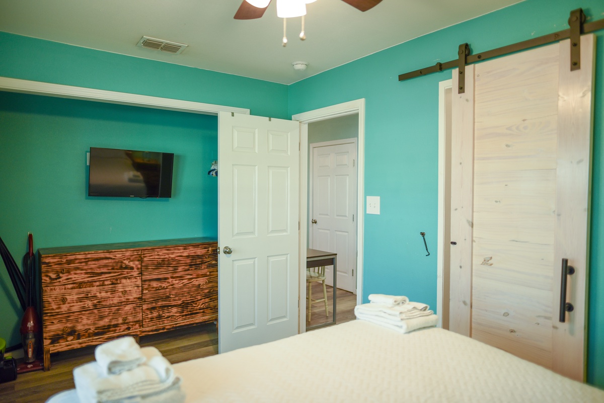 Relax in your vibrant bedroom featuring bold turquoise walls, rustic wood furnishings, and a spacious bathroom with barn door charm.