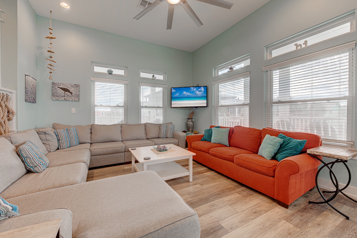 Sink into plush sectional seating with vibrant coral accents in your bright living space, complete with coastal-themed decor and entertainment center for perfect relaxation.