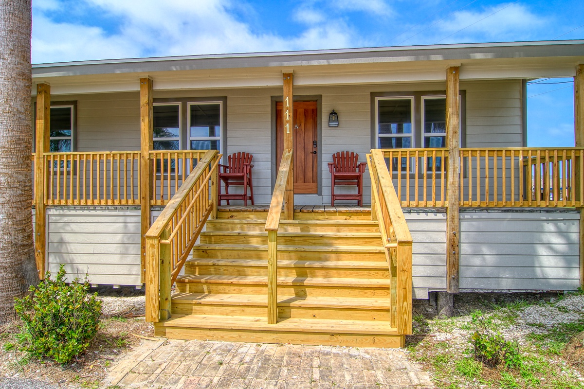 Charming coastal cottage with welcoming wraparound porch and bright red Adirondack chairs for relaxing outdoors.