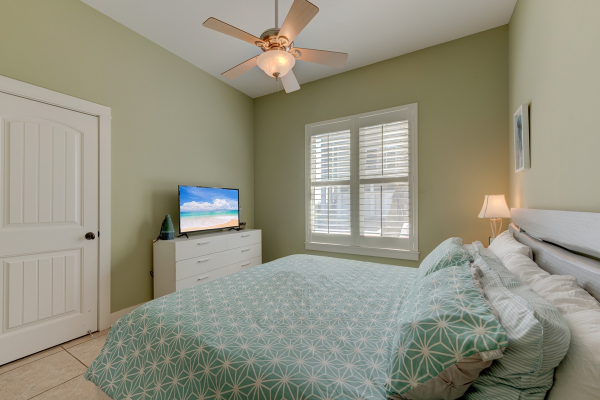 Unwind in your peaceful bedroom with soft green tones and modern comfort, where tropical dreams await on the TV screen.