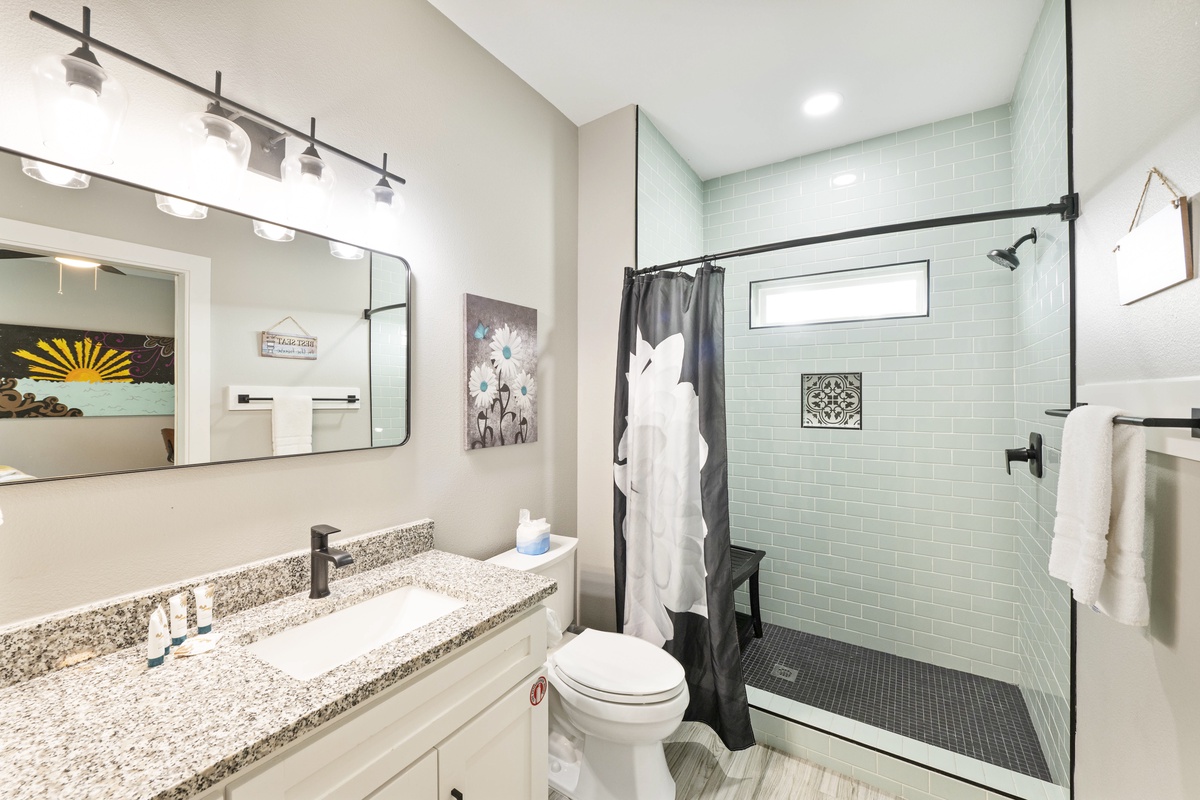 Refresh in your modern bathroom featuring a spacious tiled shower and elegant granite vanity, perfectly lit for your daily rituals.