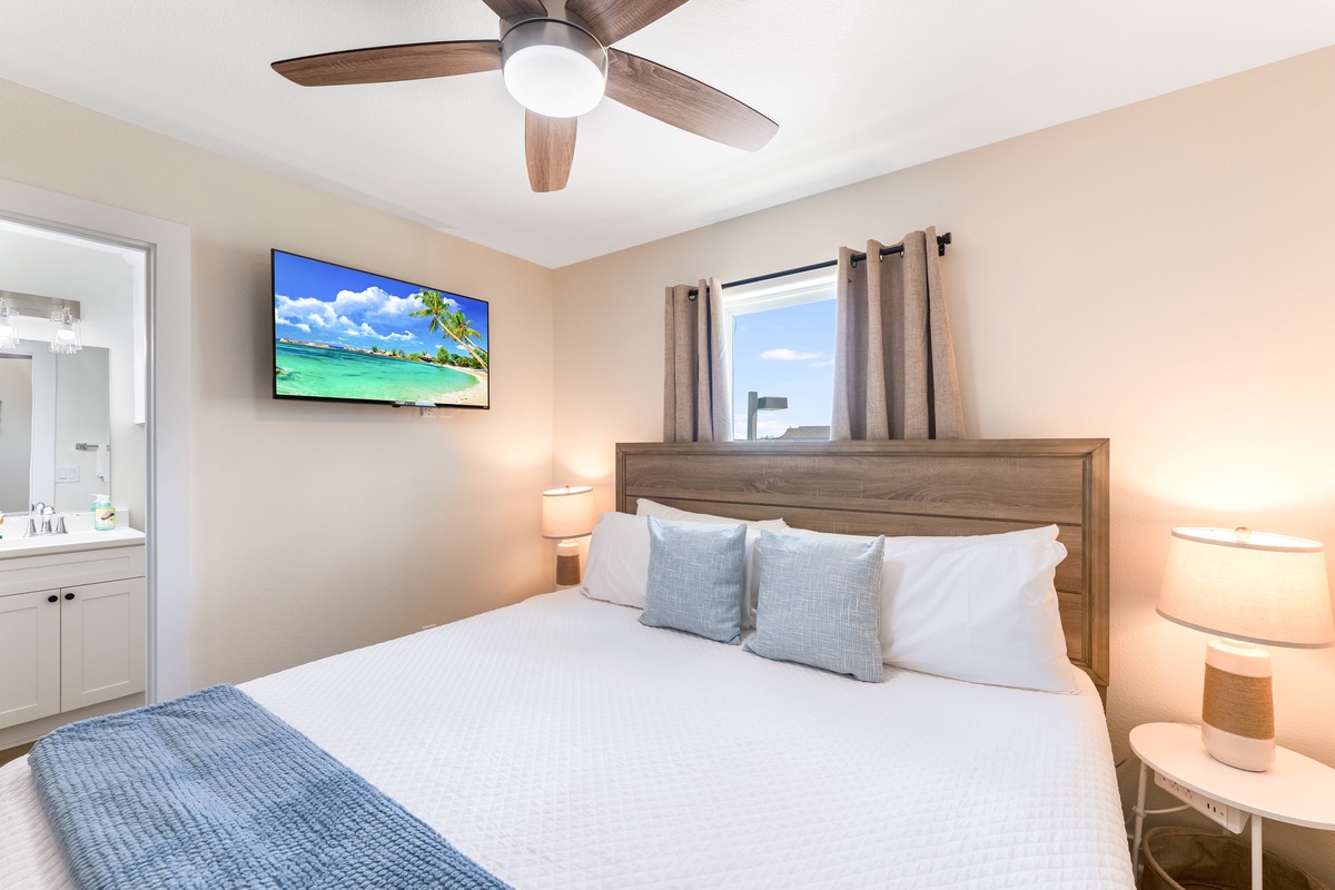 Unwind in your serene bedroom with plush bedding, ceiling fan, and tropical TV ambiance for perfect relaxation.