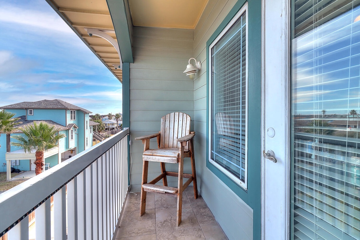 Step onto your private balcony where a cozy chair awaits your morning coffee ritual, overlooking charming coastal homes.