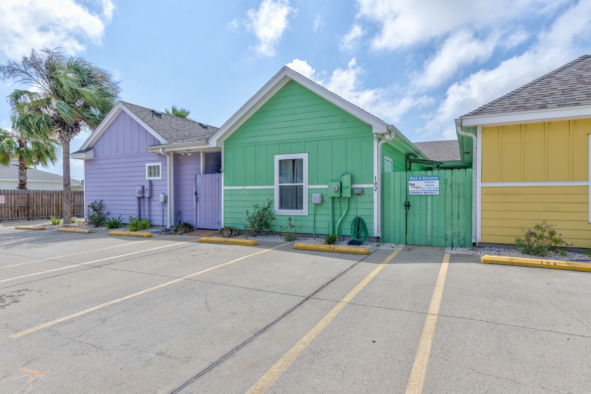 Colorful beach cottages create a cheerful arrival experience with convenient parking spaces and tropical palm trees setting the coastal scene.