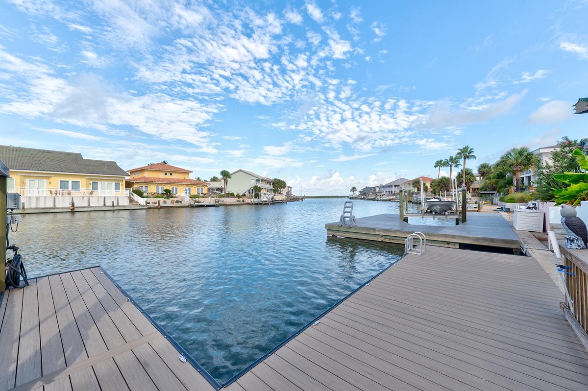 A waterfront property featuring a private dock on a peaceful canal, surrounded by palm trees and neighboring homes under a beautiful blue sky.