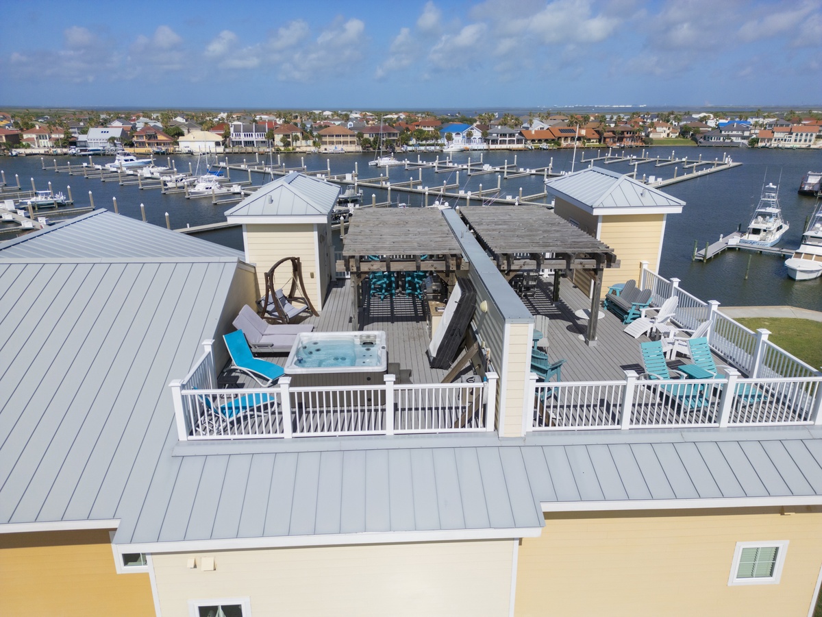 Coastal property with rooftop deck featuring hot tub, overlooking a marina and residential waterfront community.
