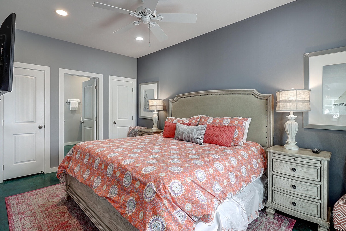 Your serene master bedroom features luxurious coral bedding, elegant nightstand lamps, and soothing blue-gray walls for the perfect restful retreat.