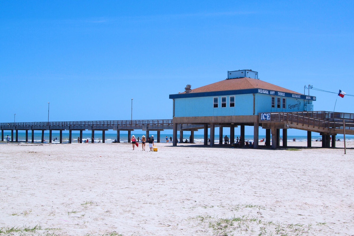 Beautiful sandy beach with historic fishing pier stretching into clear blue waters, perfect for seaside walks and coastal exploration.