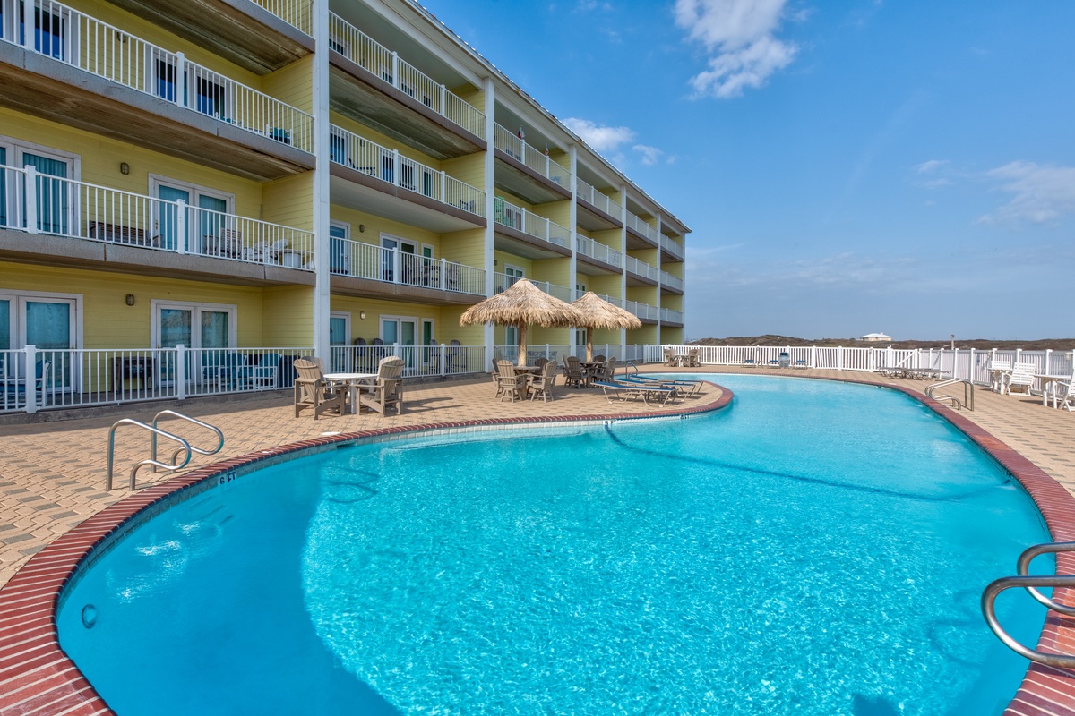 The oceanfront pool deck features ample space to lounge under the sun, with a thatched palapa providing cool shade and comfortable seating perfect for your beach vacation.