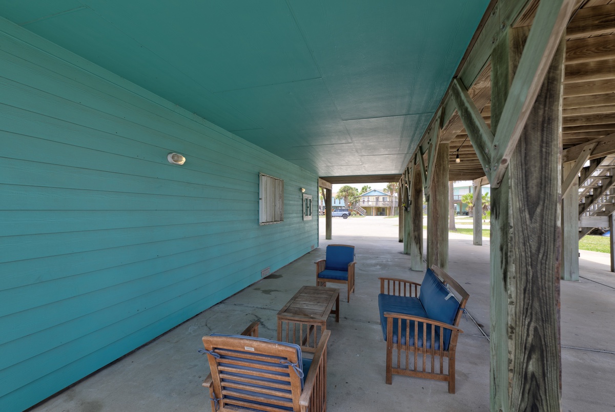 This covered breezeway with comfortable seating offers a relaxing spot for you to unwind after a day of exploring, framed by charming turquoise coastal architecture.