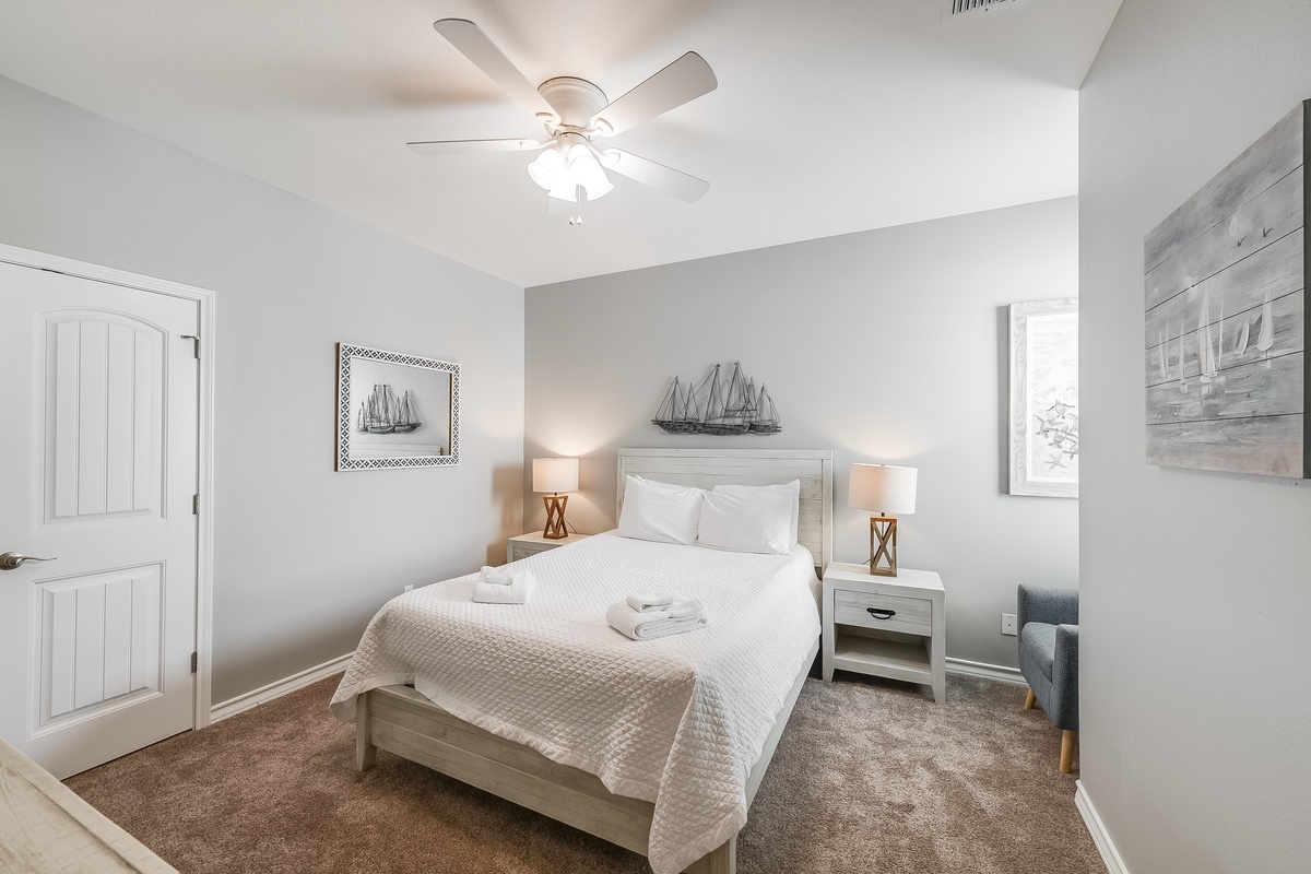 Drift off to sleep in your serene bedroom, featuring plush linens, coastal art, and a gentle ceiling fan for perfect comfort.