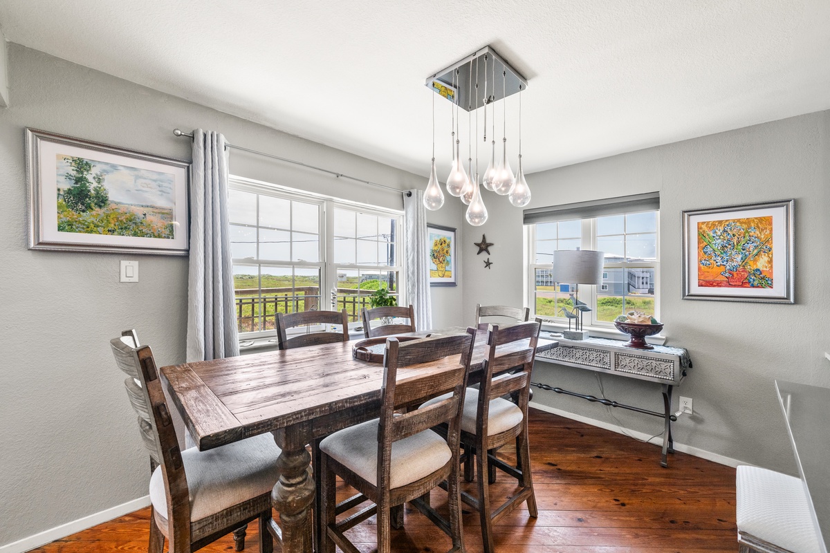 Gather around a beautiful rustic table beneath a modern chandelier, with natural light pouring in through large windows framing peaceful neighborhood views.