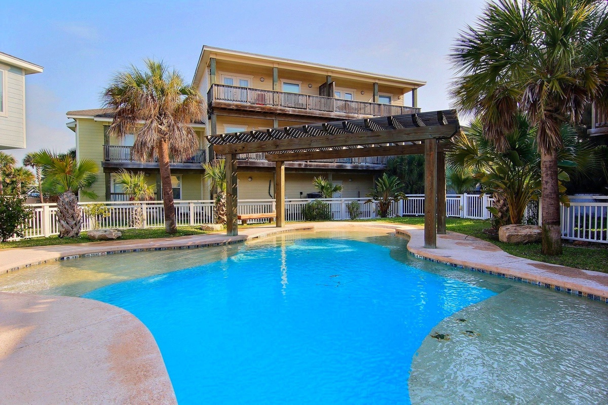 Dive into your private paradise with crystal-clear waters surrounded by swaying palm trees and a pergola for perfect poolside lounging.