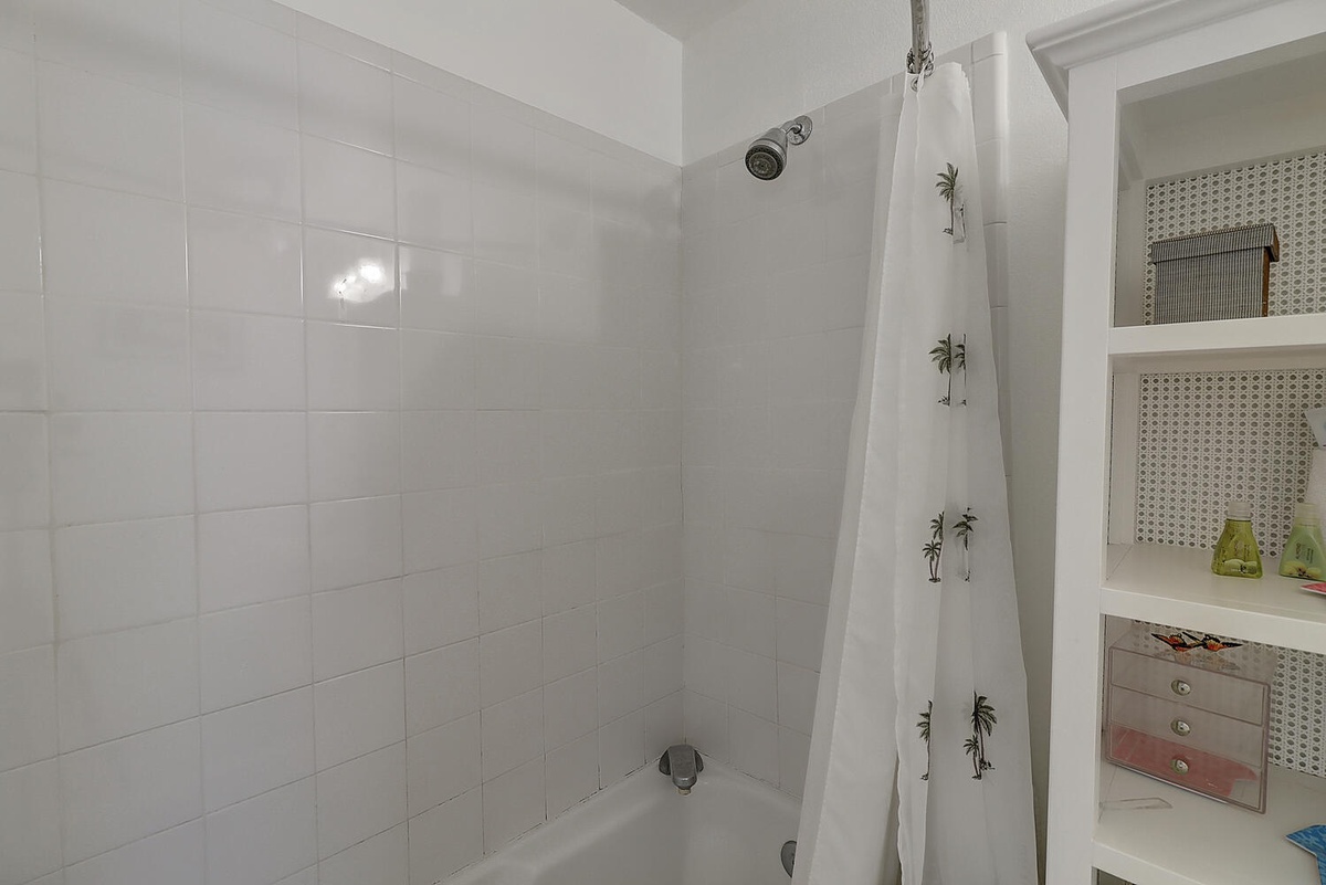 Step into your bright, tiled shower-tub combo with tropical palm curtain and built-in storage for all your essentials.