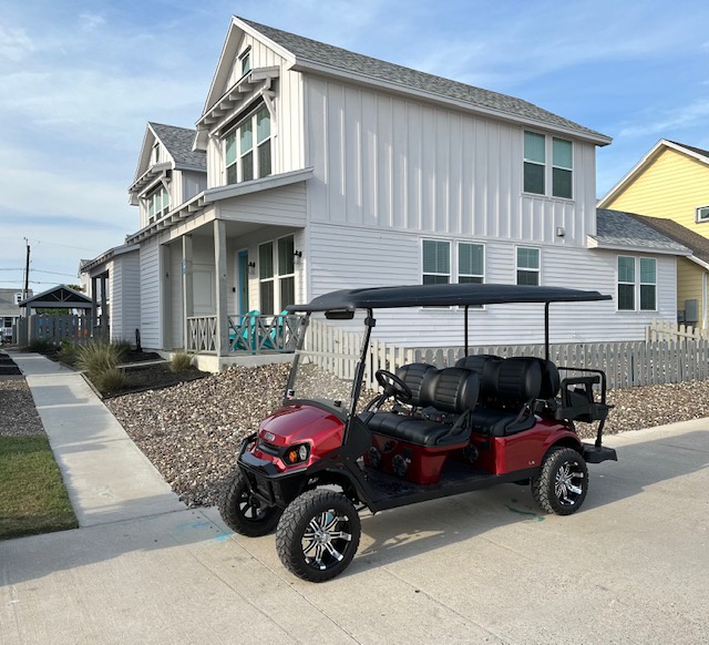 Modern two-story beach house with white siding and coastal charm, featuring convenient golf cart parking for easy neighborhood exploration.