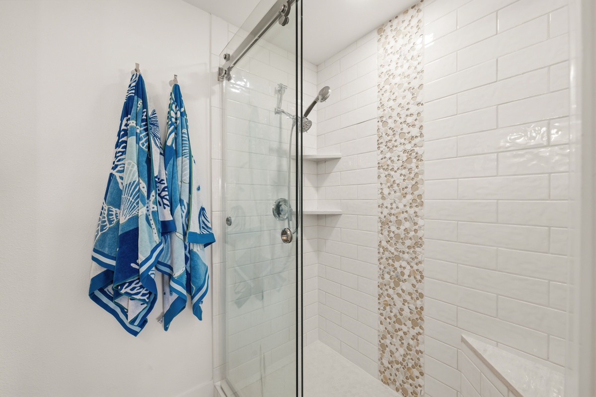Your stylish bathroom features a spacious walk-in shower with modern tile work and a decorative pebble accent strip. Beach towels are ready for your coastal getaway.