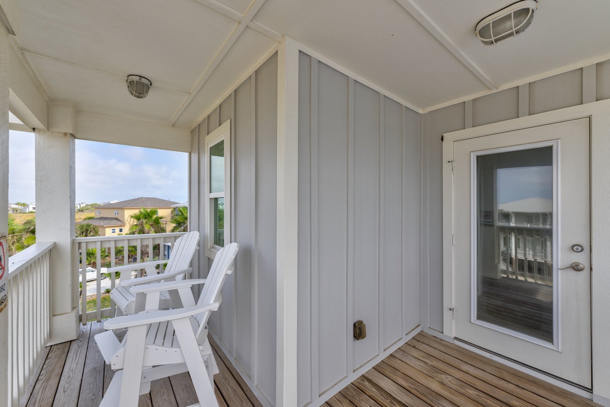 Relax on your private covered balcony with comfortable white chairs and scenic neighborhood views - perfect for morning coffee or evening unwind.