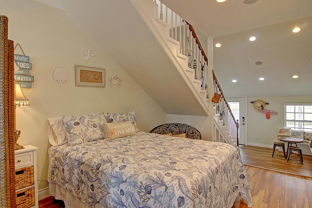 Your cozy bedroom features charming coastal decor and warm hardwood floors, with a staircase leading to additional space above.