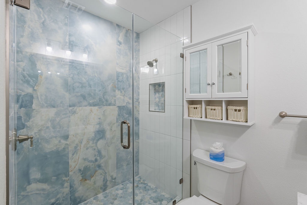 Step into your spa-like bathroom featuring a stunning marble shower with glass doors and organized storage baskets for your comfort.