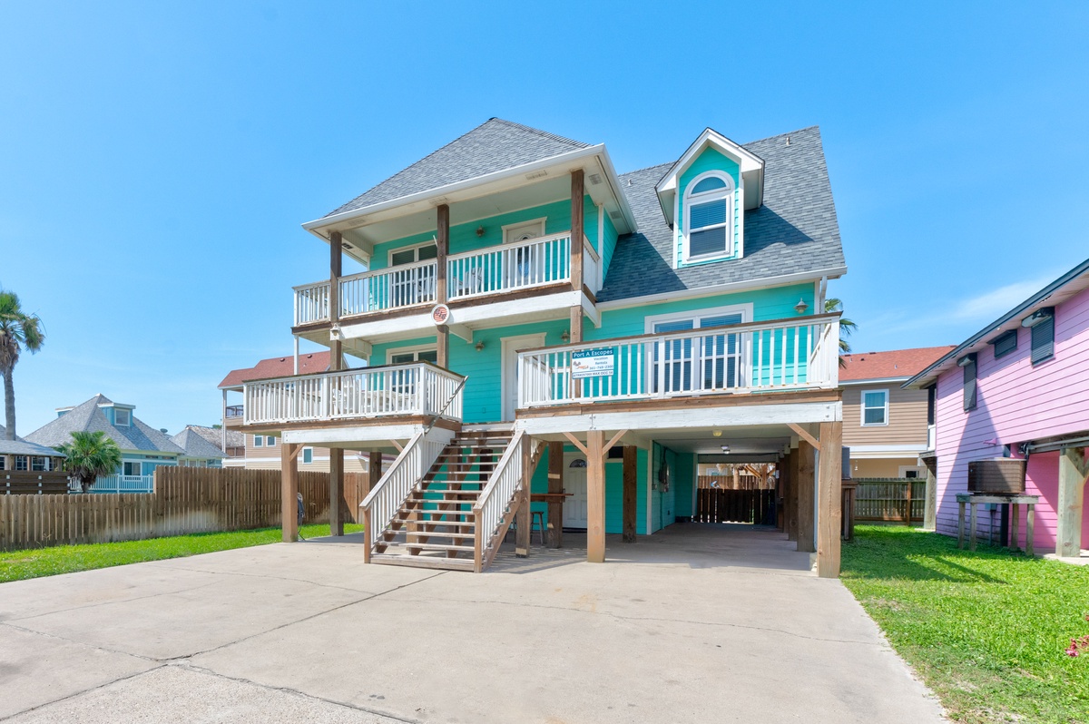 Vibrant turquoise beach house with multiple balconies and covered parking in a colorful coastal neighborhood.