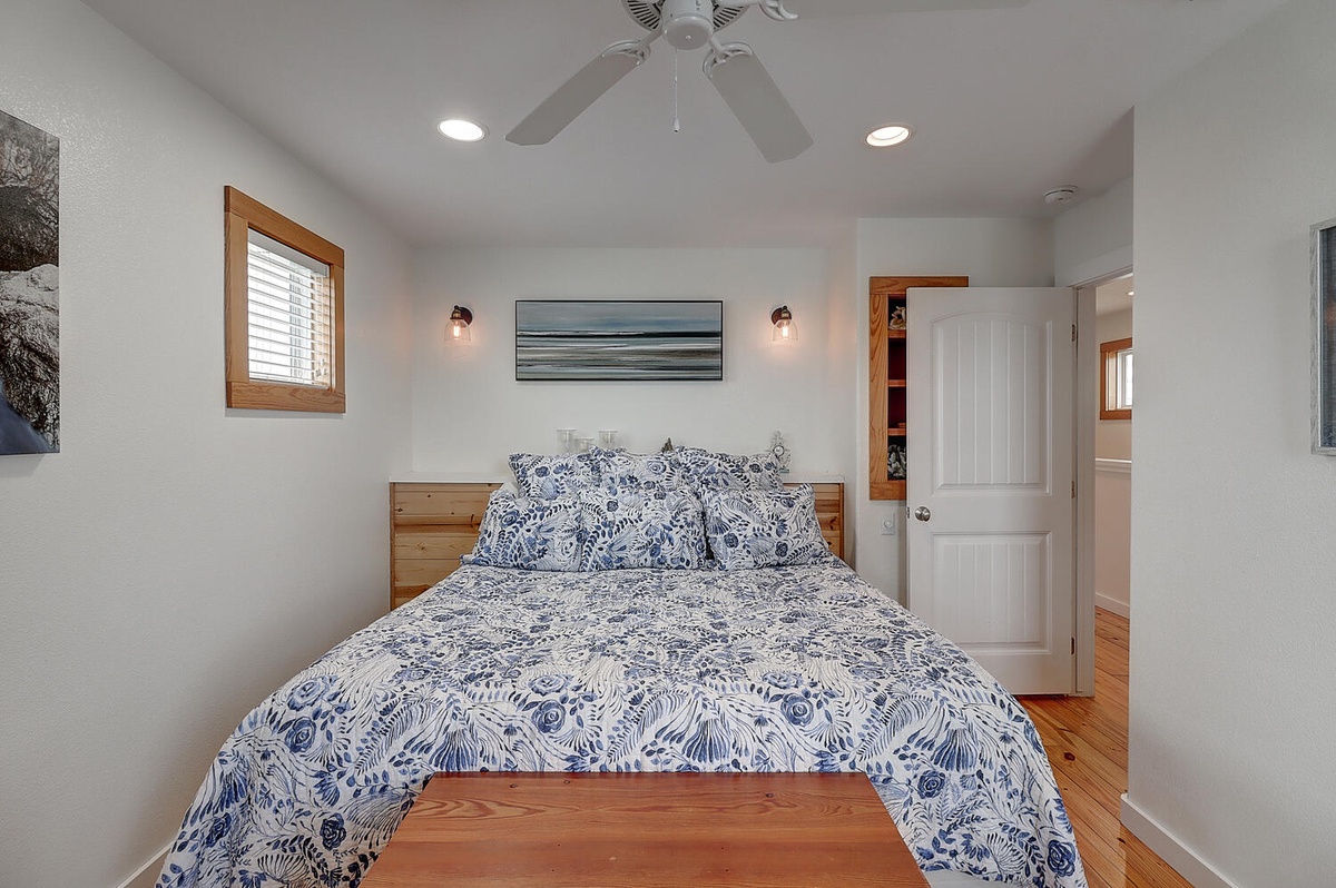 Drift off in your cozy bedroom featuring beautiful blue botanical linens, warm wood touches, and soothing coastal artwork overhead.