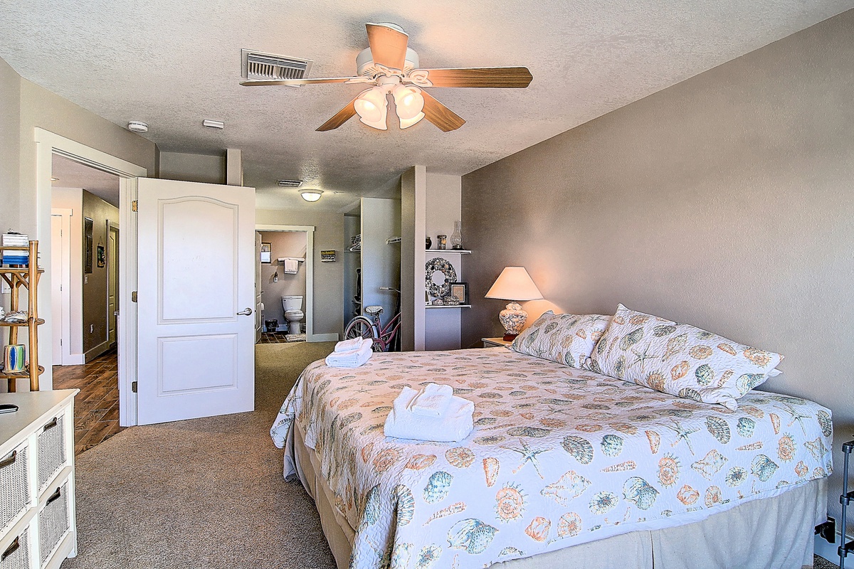 Relax in your spacious bedroom featuring coastal bedding, gentle ceiling fan, and thoughtful touches like fresh towels awaiting your arrival.