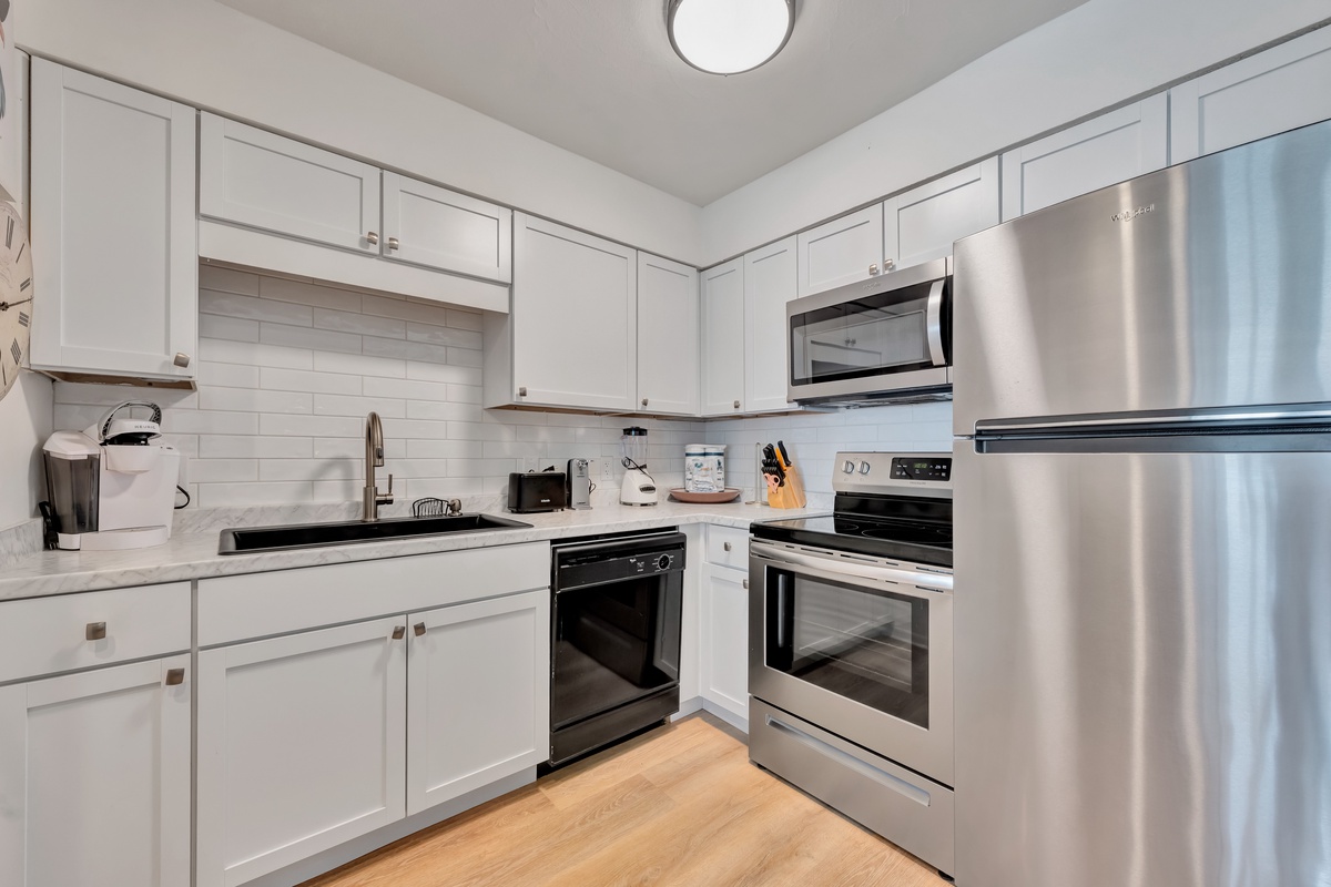 Your fully equipped modern kitchen awaits with stainless steel appliances, sleek white cabinetry, and warm hardwood floors perfect for preparing meals.