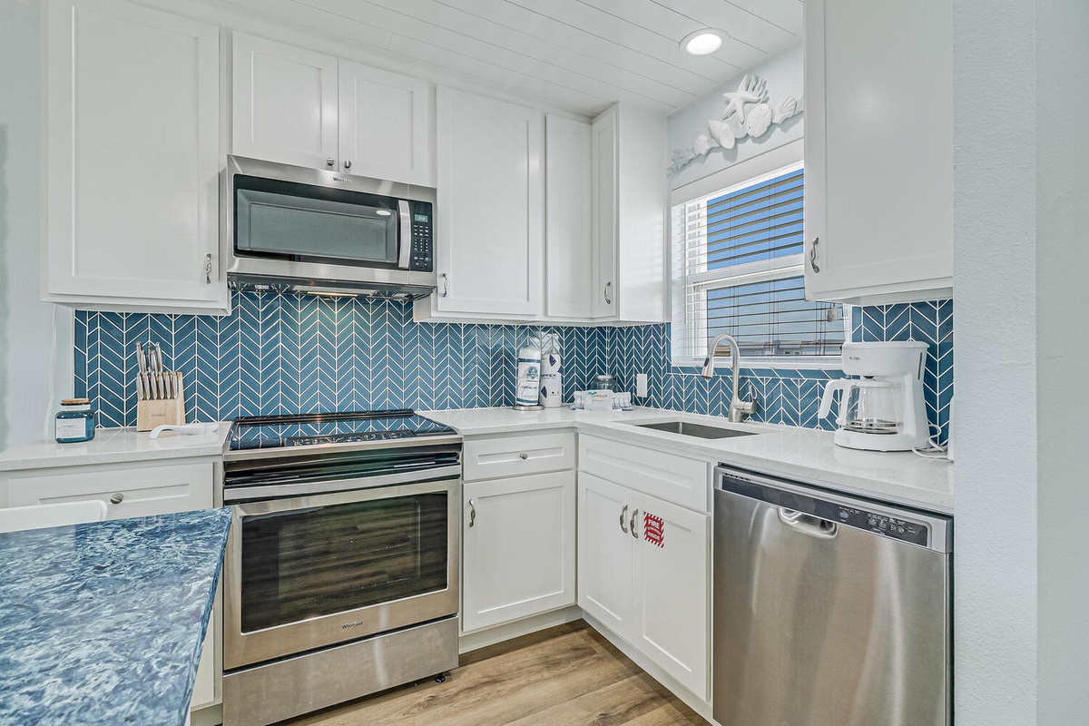 Your bright kitchen features white cabinetry, stunning blue herringbone backsplash, and modern stainless steel appliances for memorable vacation meals.