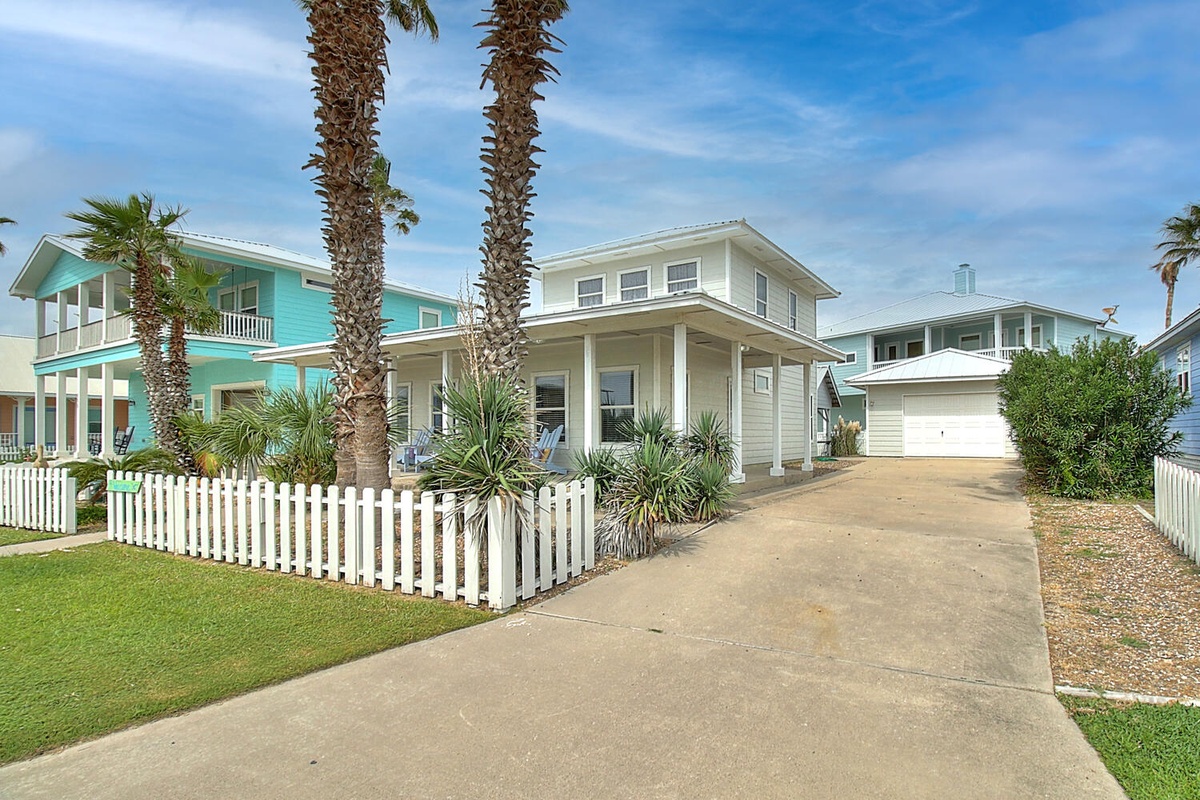 Charming coastal home with white picket fence, palm trees, and tropical landscaping in a peaceful beachside neighborhood.