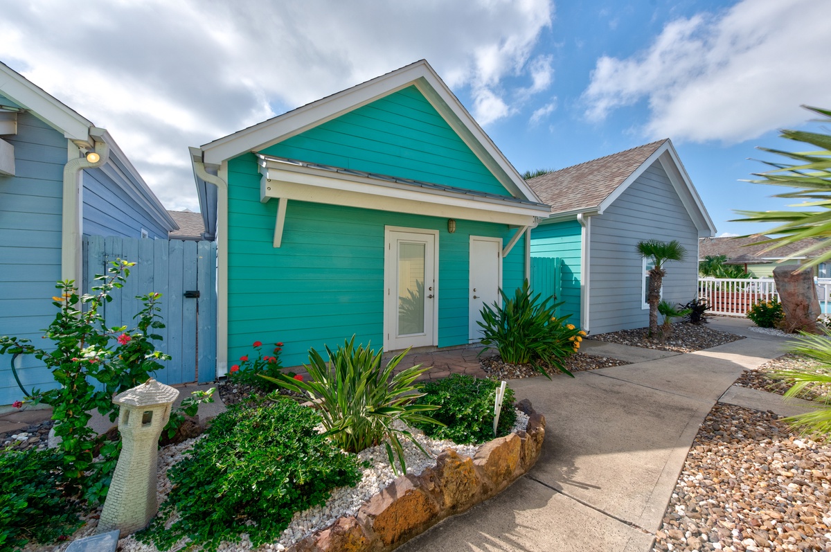 Charming turquoise cottage with tropical landscaping and welcoming front entrance in a peaceful neighborhood setting.