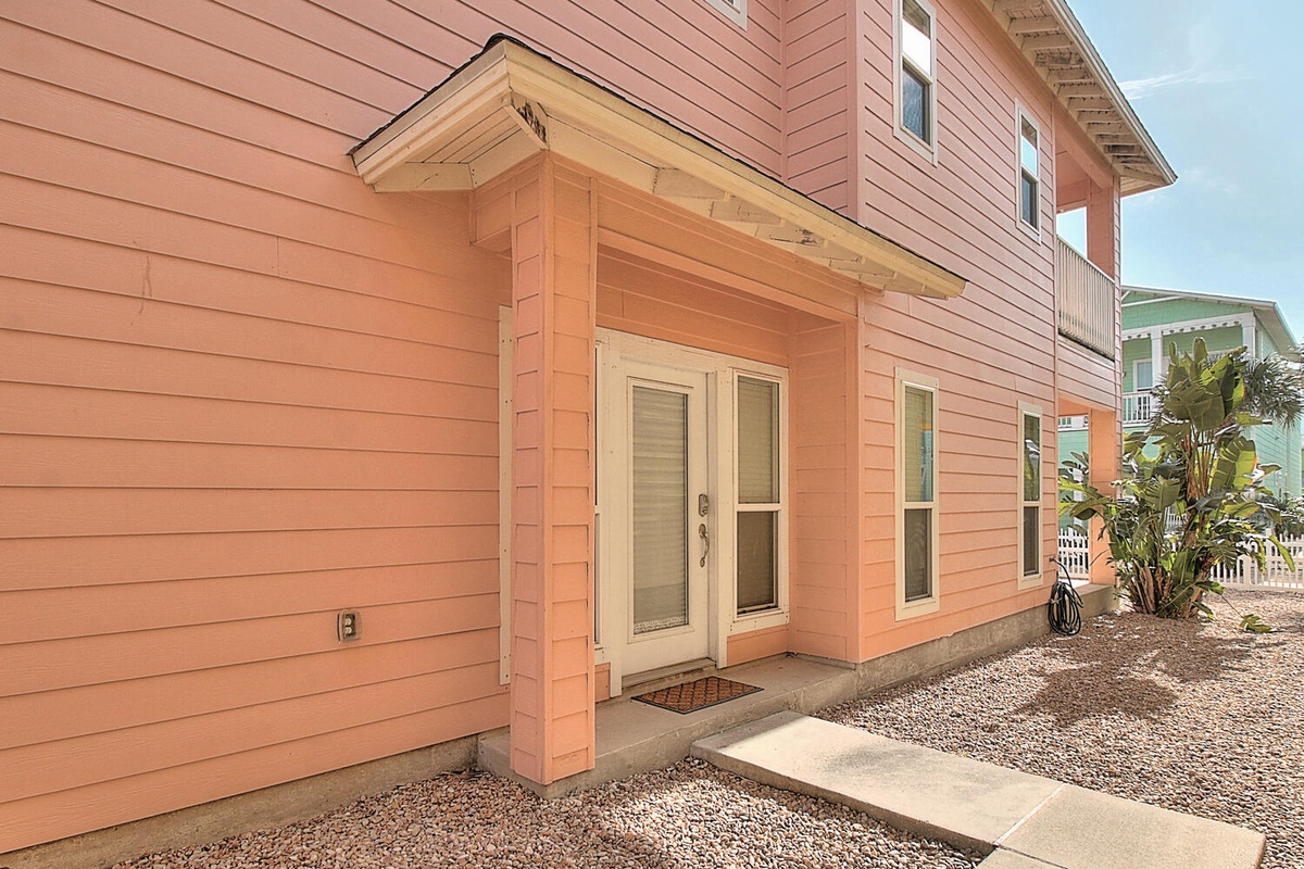 Charming coral-colored beach house with covered entrance and tropical landscaping creates a welcoming coastal arrival experience.