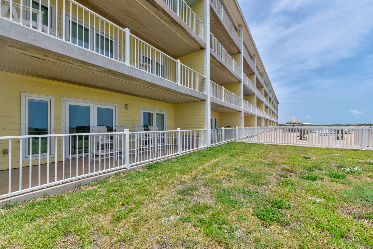 A multi-story beachfront building offers direct access to grassy dunes and oceanfront views. Ground-level units feature private patios, while upper floors have spacious balconies overlooking the coast.