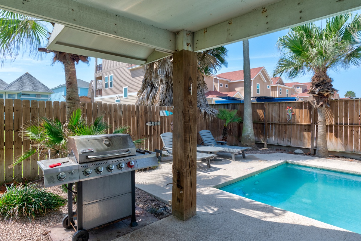 Your private backyard paradise awaits with a sparkling pool, covered patio, and BBQ grill surrounded by swaying palms.