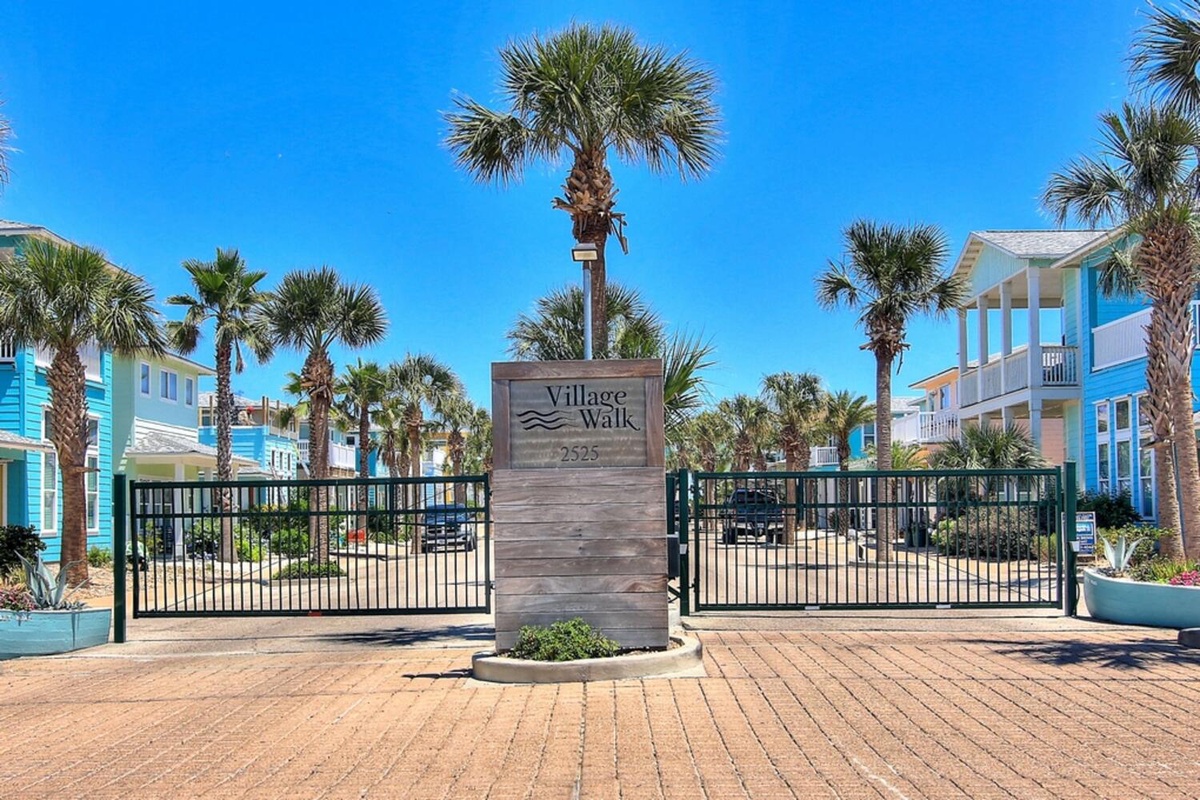 Village Walk community entrance showcases tropical landscaping and coastal architecture against clear blue skies.