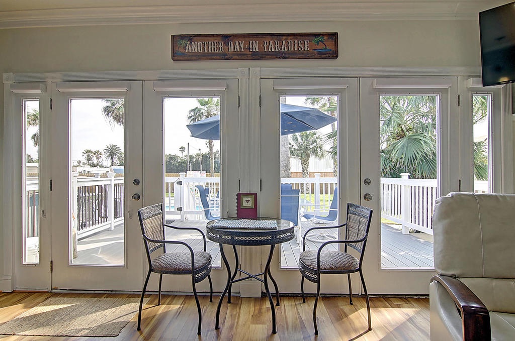 Your bright dining nook opens to a tropical balcony where palm trees sway beyond white railings, creating the perfect spot for morning coffee.