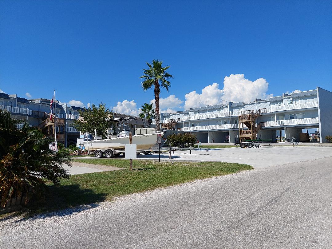 Modern waterfront property complex featuring clean white buildings and tropical palm trees under brilliant blue skies.