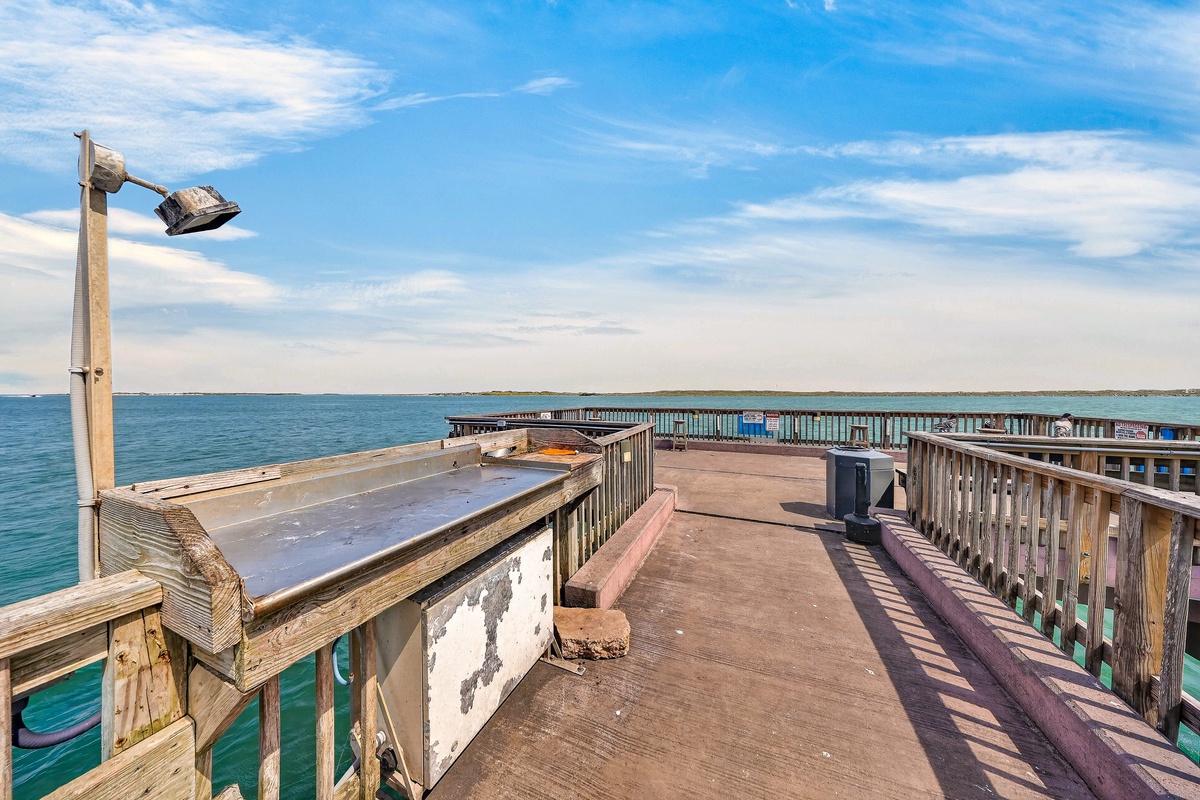 A weathered fishing pier stretches into turquoise waters, offering views of the surrounding coastline and blue horizon—a peaceful spot near the property.