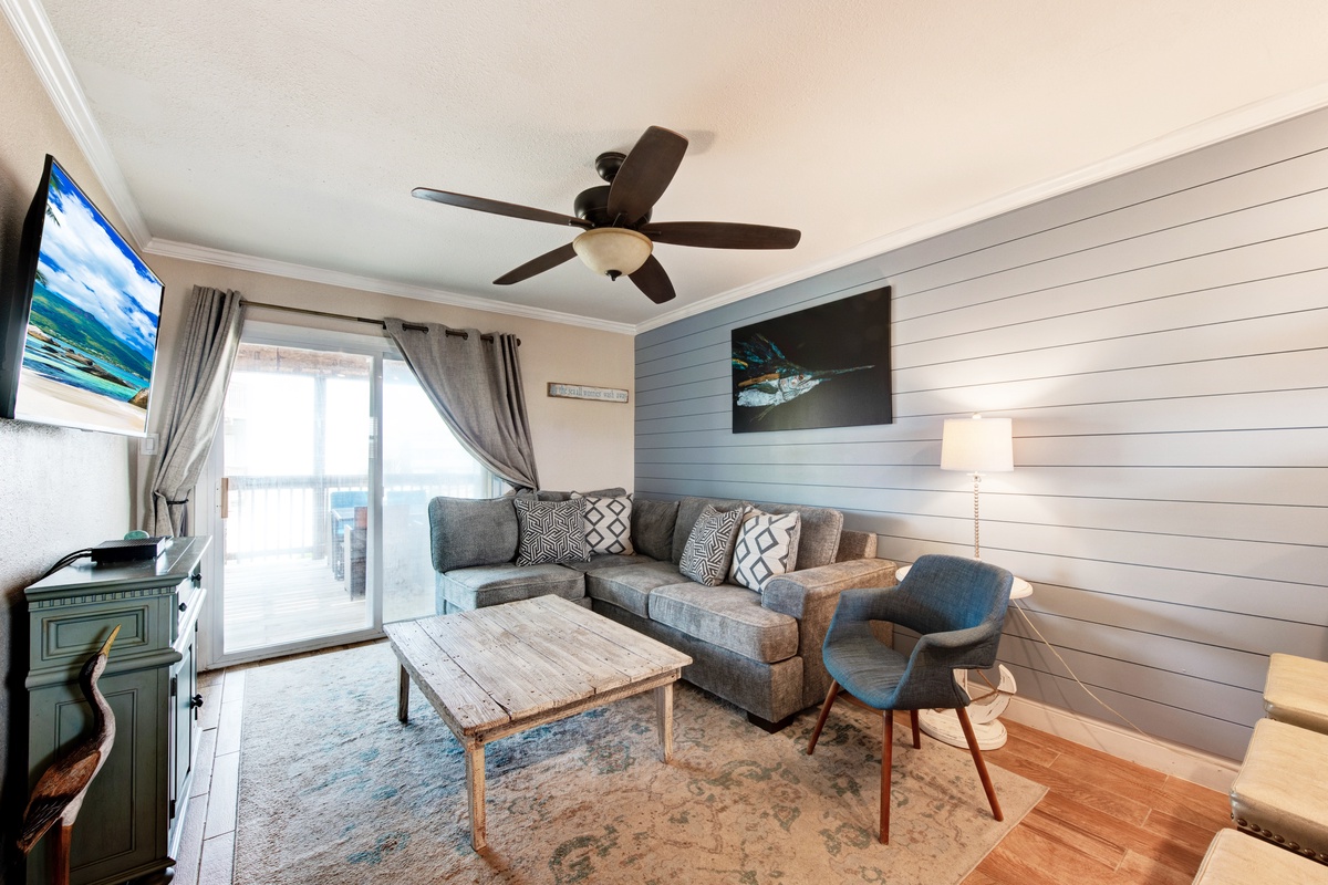 Relax in your coastal-inspired living room featuring a cozy sectional, rustic coffee table, and charming shiplap accent wall with ceiling fan overhead.