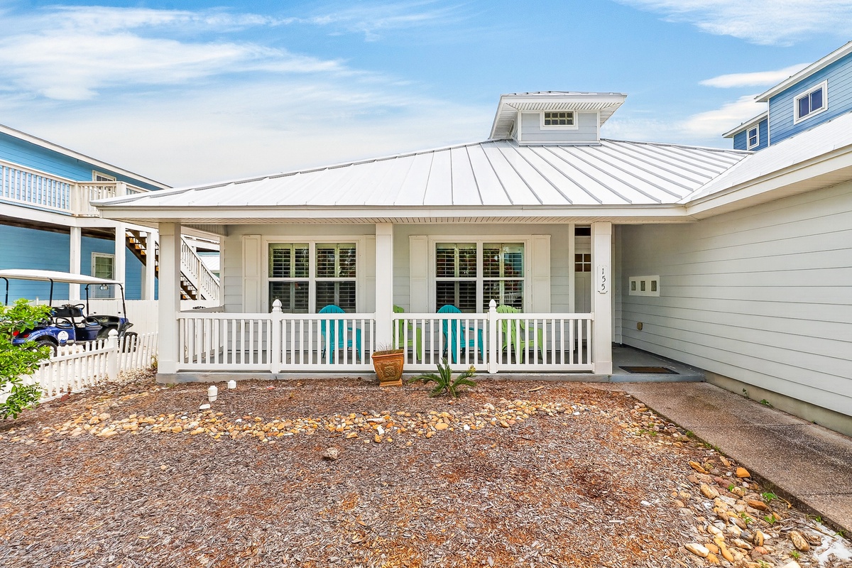 Charming coastal cottage featuring a welcoming front porch with white railings and metal roofing in a peaceful residential neighborhood.