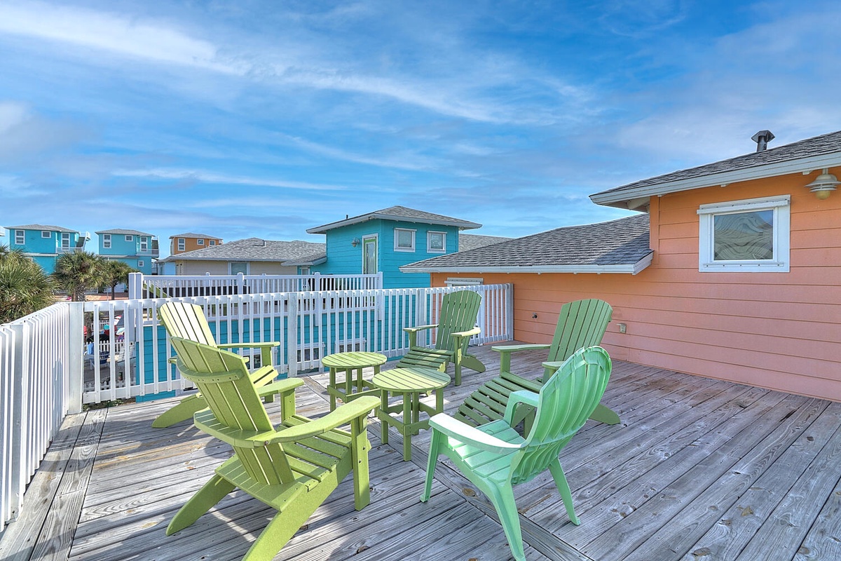 Relax in colorful Adirondack chairs on your private deck, surrounded by vibrant coastal homes under endless blue skies.