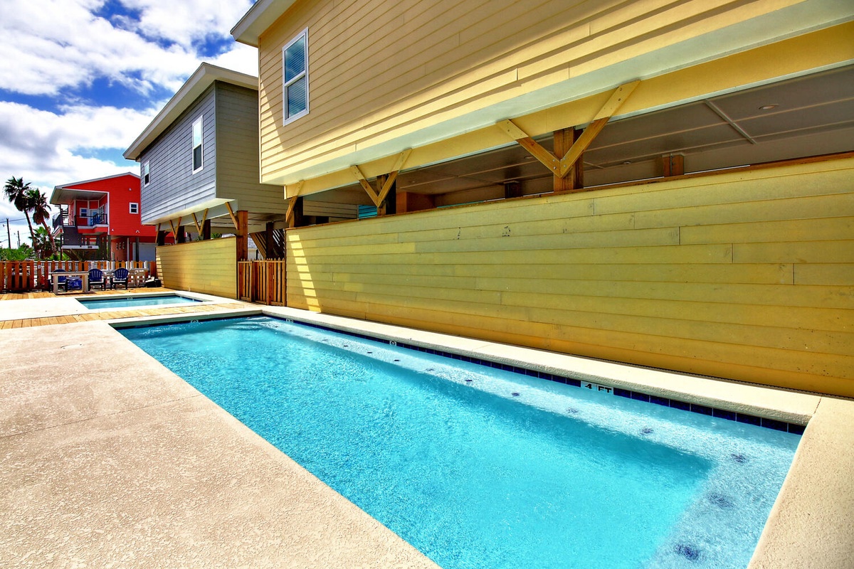 Dive into your private pool, surrounded by vibrant coastal homes and shaded by a wooden pergola for perfect poolside relaxation.