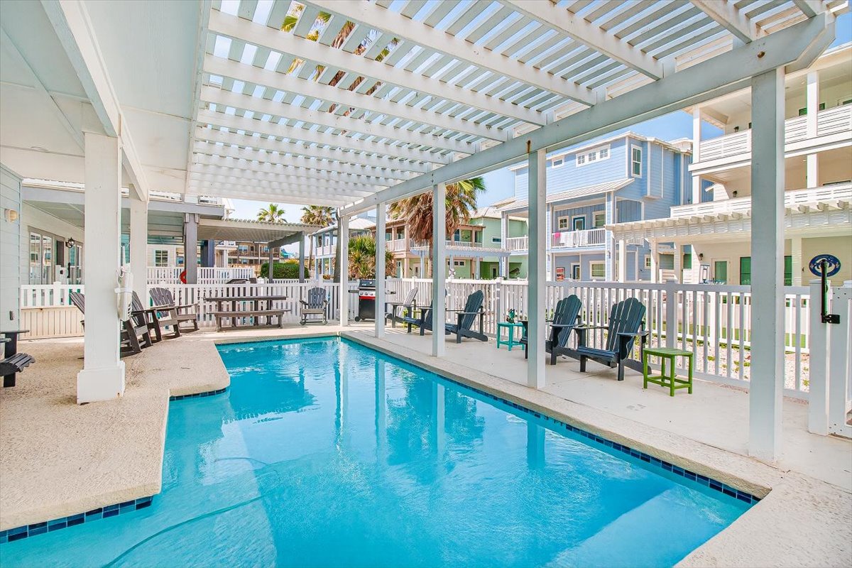 Dive into your private oasis under the covered pergola, where comfortable seating surrounds sparkling blue waters for perfect poolside relaxation.