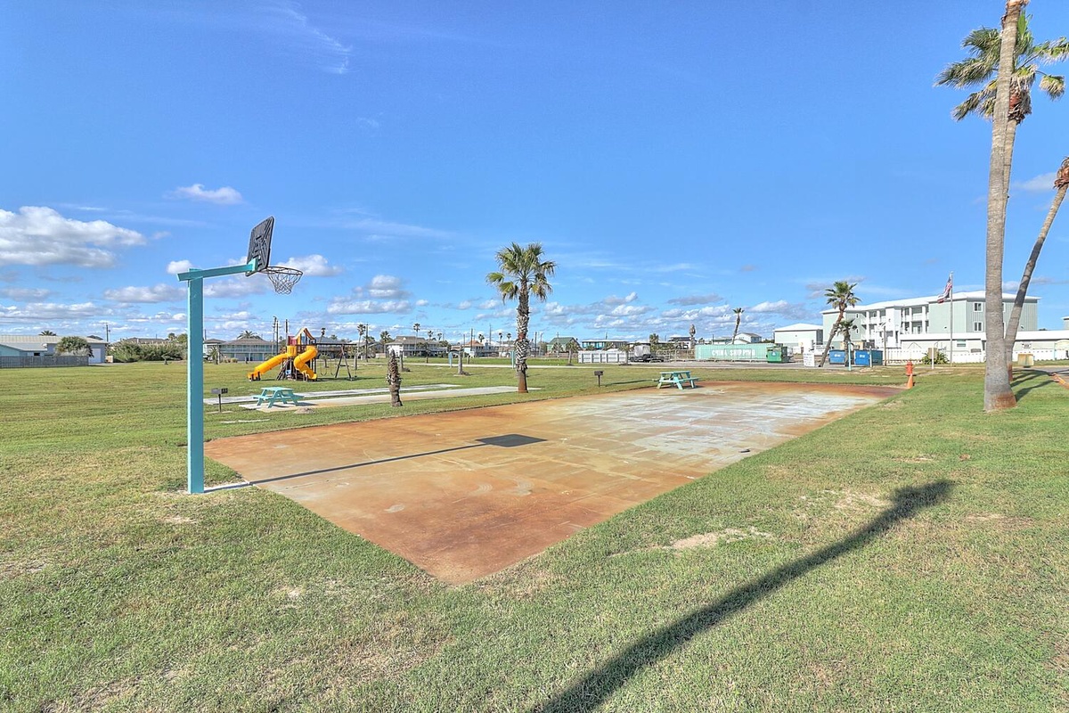 Recreation area features basketball court, playground, and palm trees in a sunny coastal setting.