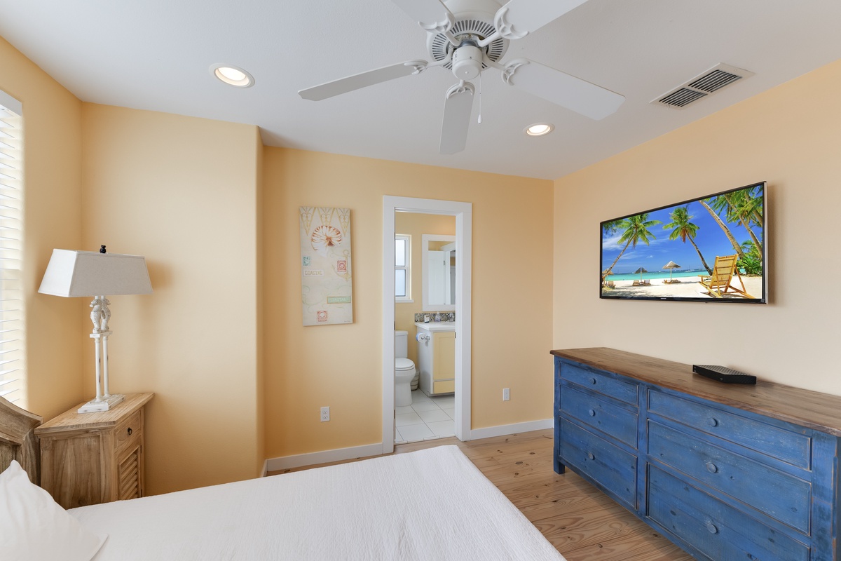 Relax in your bright bedroom featuring coastal decor, ceiling fan, and tropical TV art that sets the perfect vacation mood.
