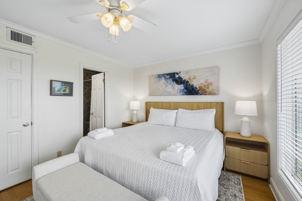 Step into your serene bedroom retreat, where plush white linens and soft lighting invite you to unwind. The gentle ceiling fan and climate control ensure your perfect comfort throughout your stay.