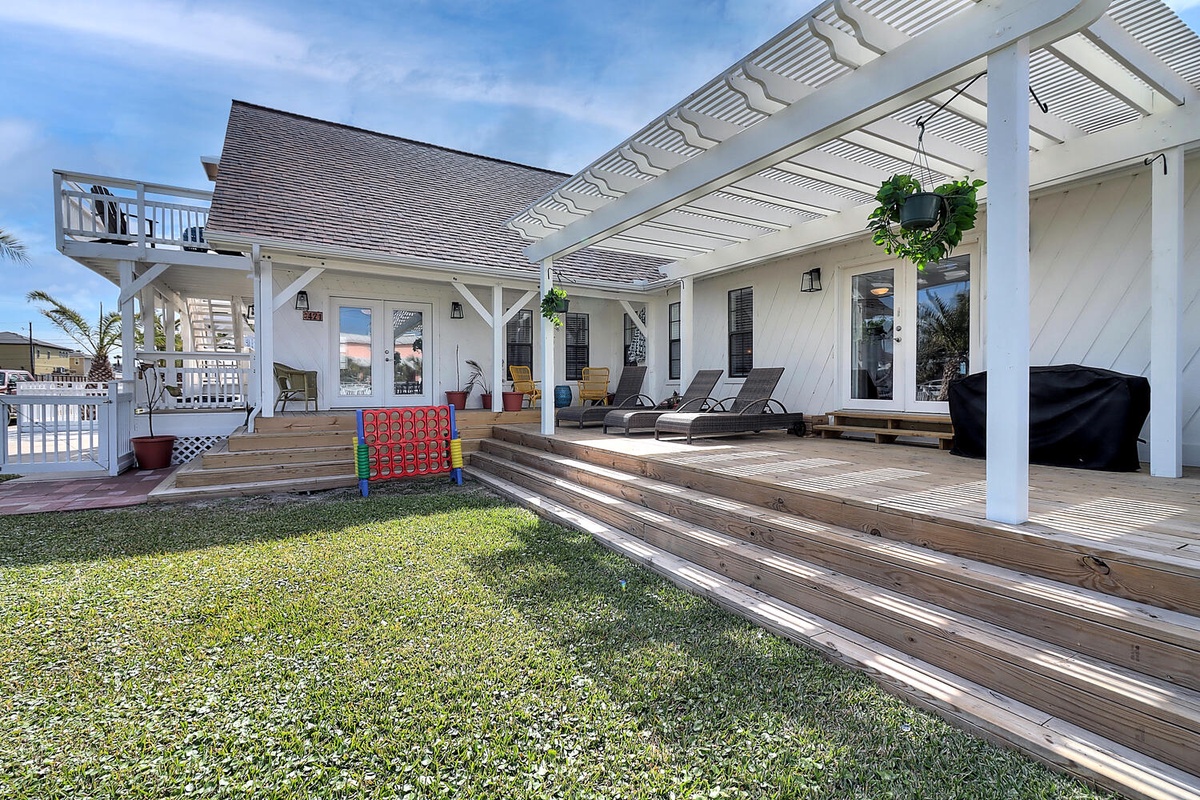 A beautiful beachside property featuring spacious covered decking, outdoor lounge chairs, and a children's play area on manicured lawn.