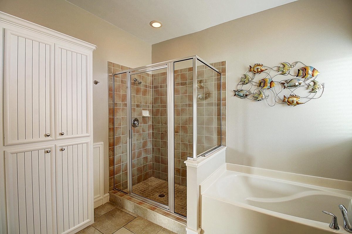 Unwind in your spa-like master bathroom featuring a glass-enclosed tiled shower, soaking tub, and elegant coastal decor.